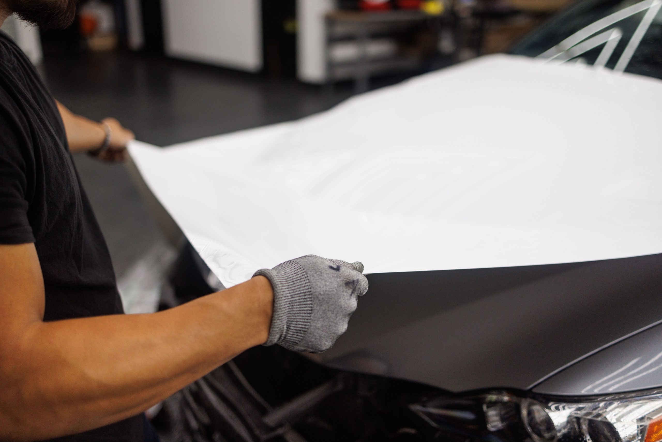 Installer applying vinyl film to a car hood, illustrating a full vehicle wrap in progress