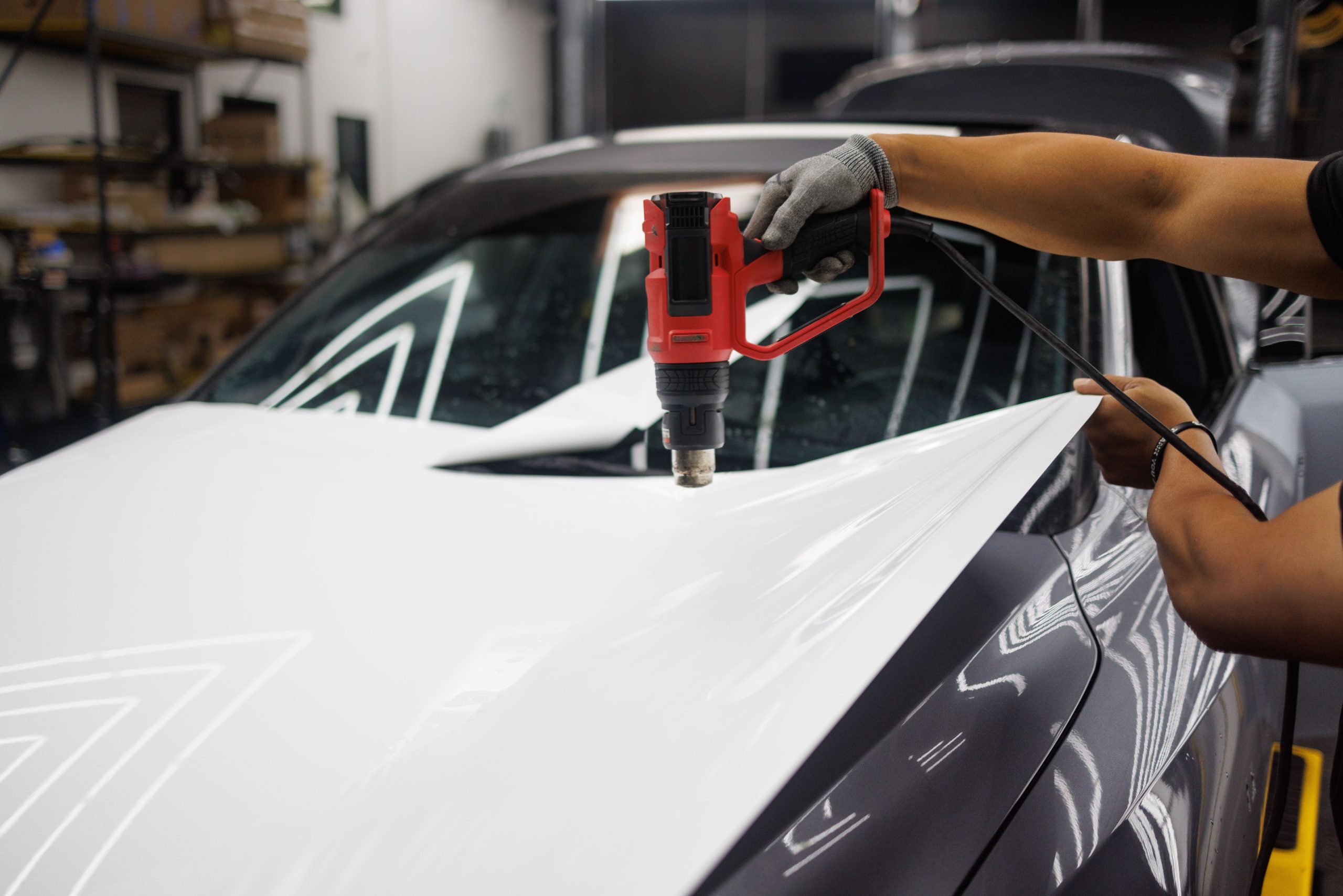Technician using a heat gun to bond vinyl wrap film to a car's body panel during installation