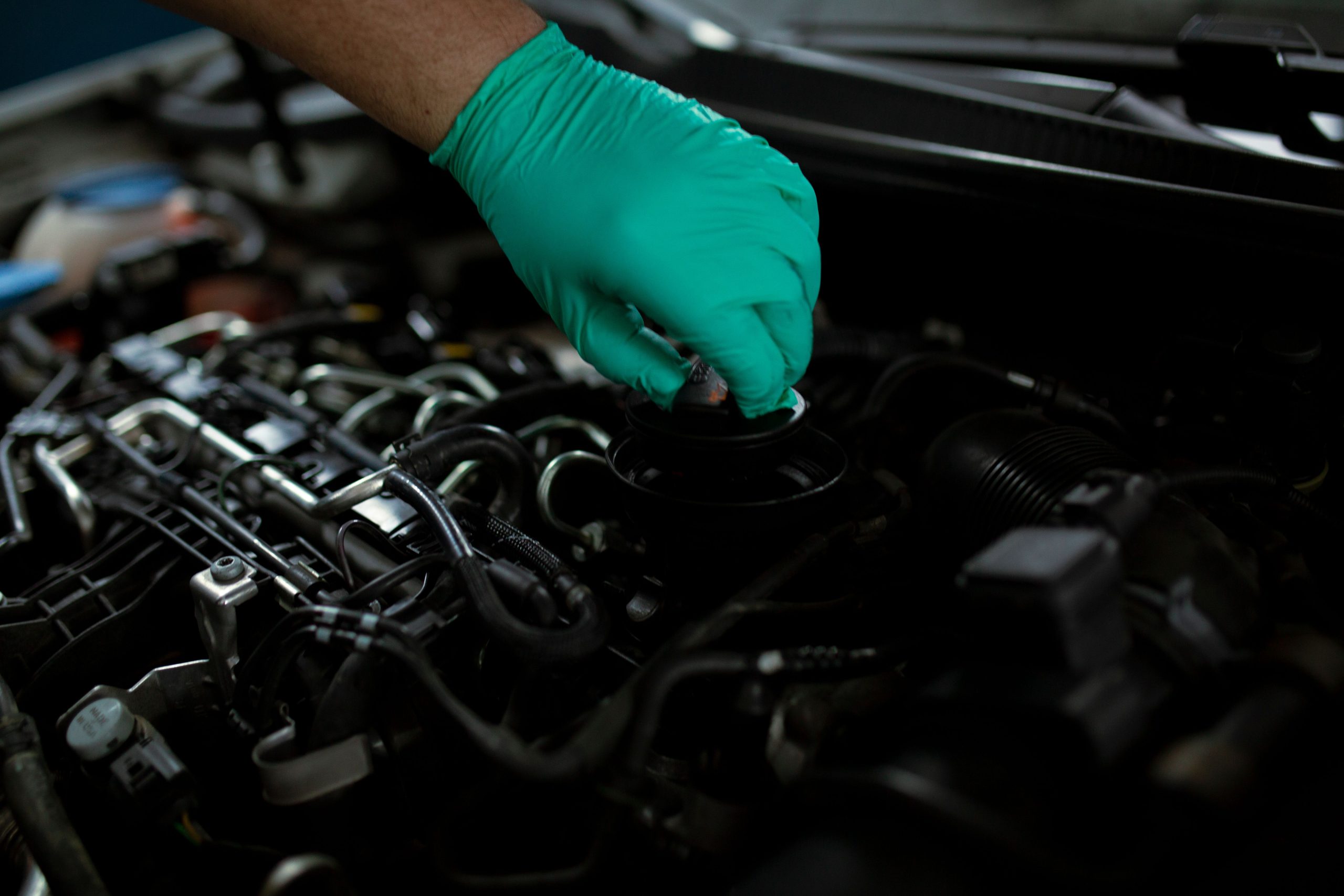Mechanic opening the oil filler cap on a car engine to inspect for a leak