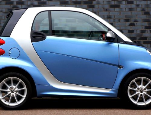 Blue Smart Fortwo microcar parked on a city street, showing its very short two-seat body