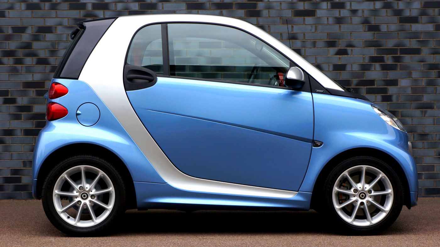 Blue Smart Fortwo microcar parked on a city street, showing its very short two-seat body