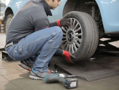 Person kneeling beside a car changing a wheel with a lug wrench