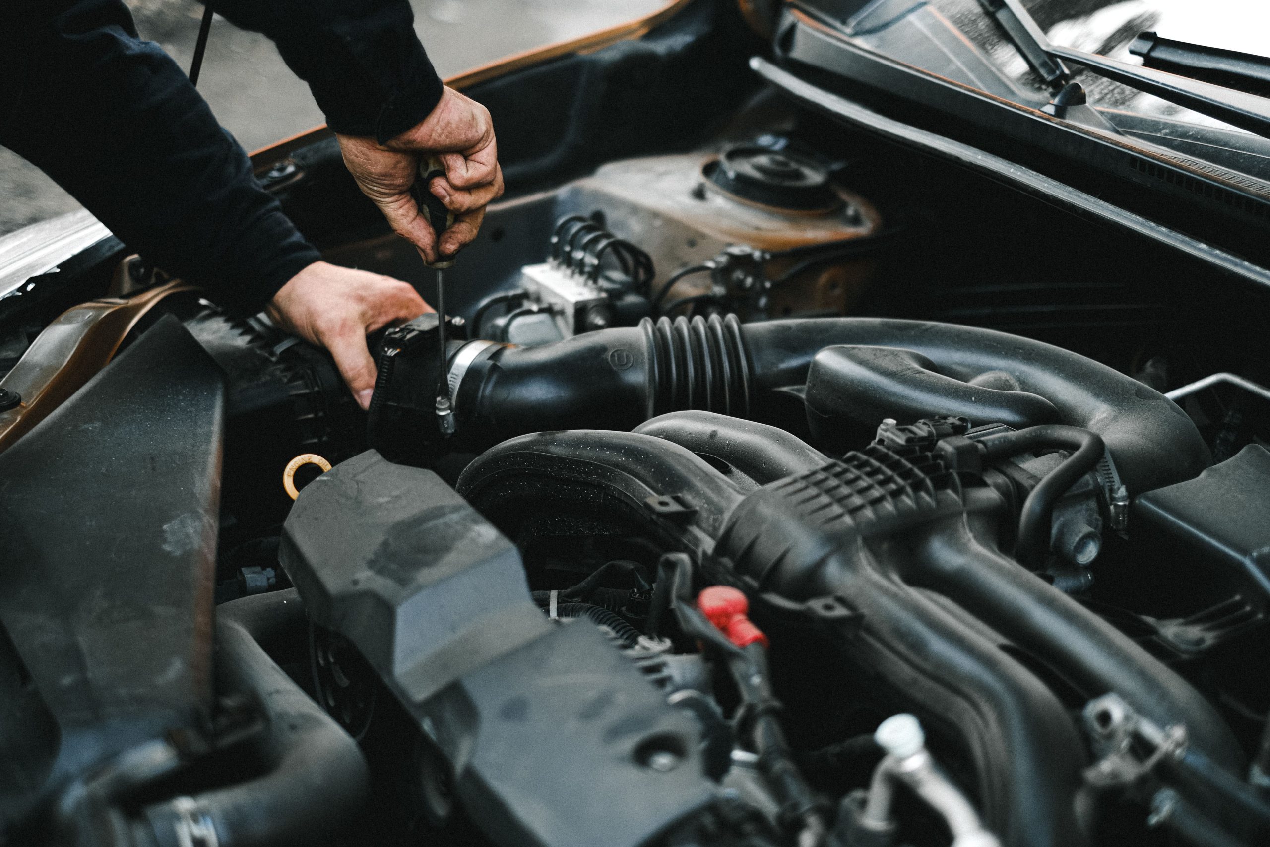 A mechanic's hands inspecting components inside a car engine bay during a maintenance check