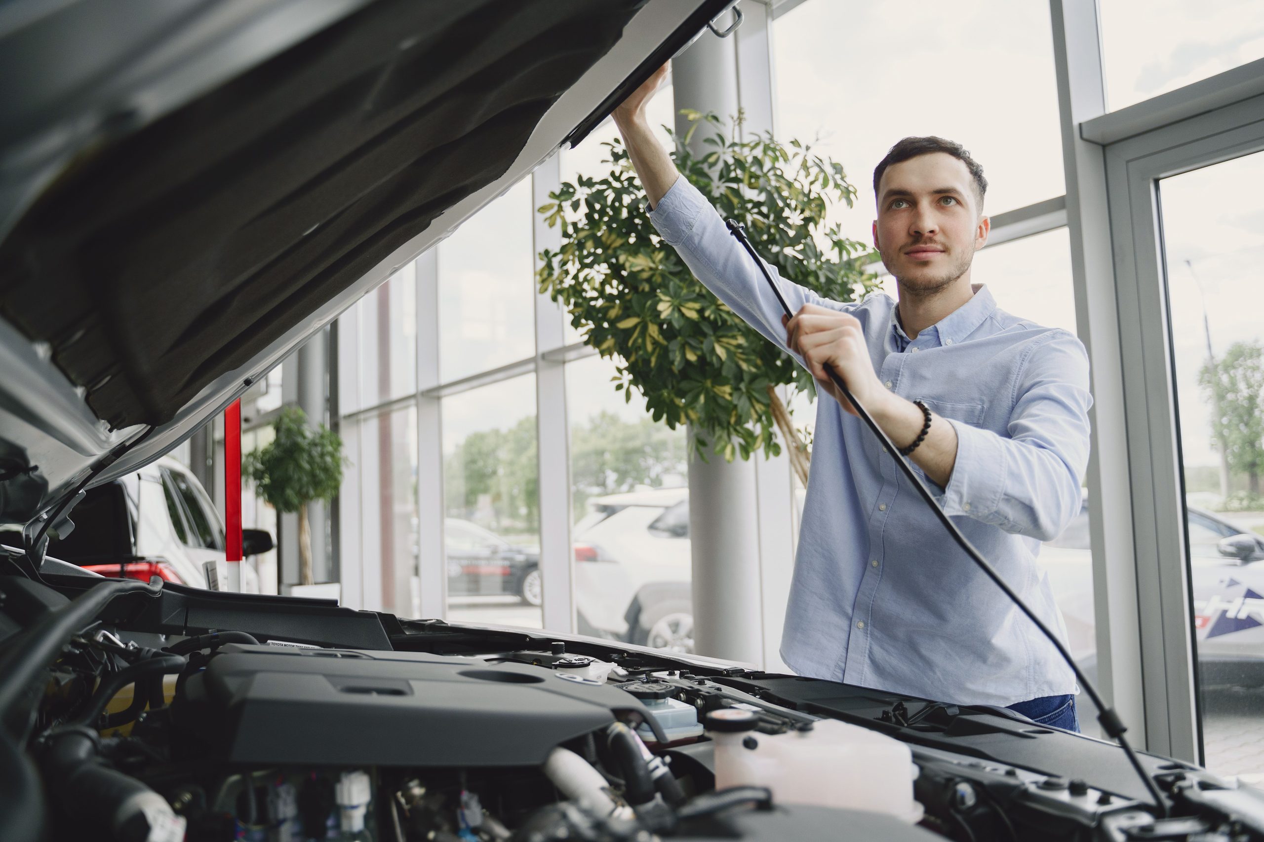 Man checking a car engine in a bright showroom