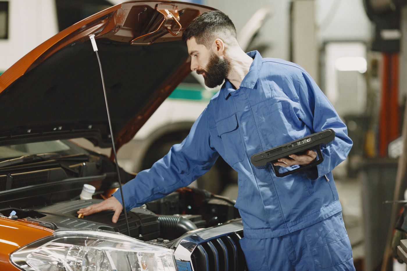 Technician inspecting a car engine under an open hood in a garage