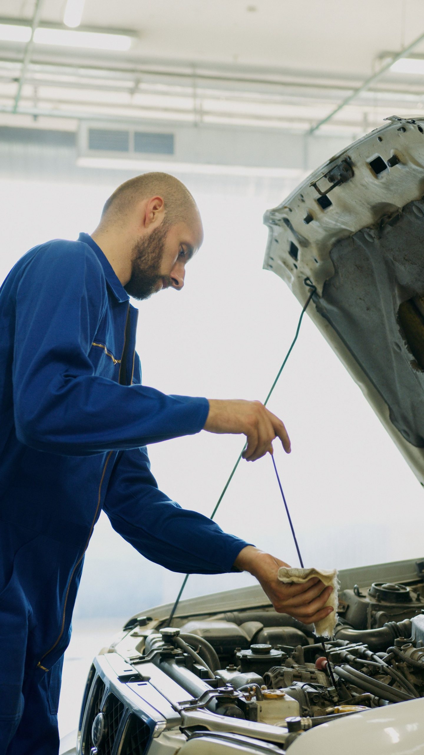 Mechanic inspecting a car engine with a dipstick in a repair shop